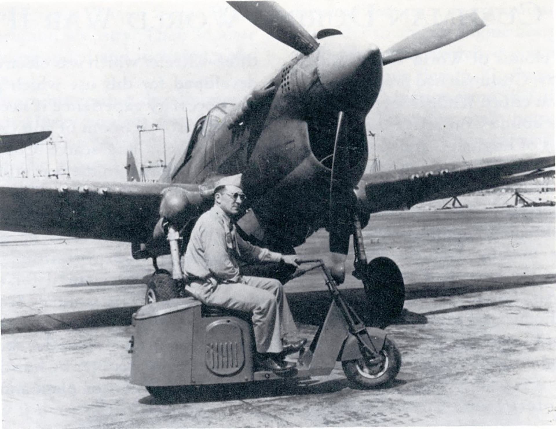 A person driving a motor scooter in front of a small aeroplane